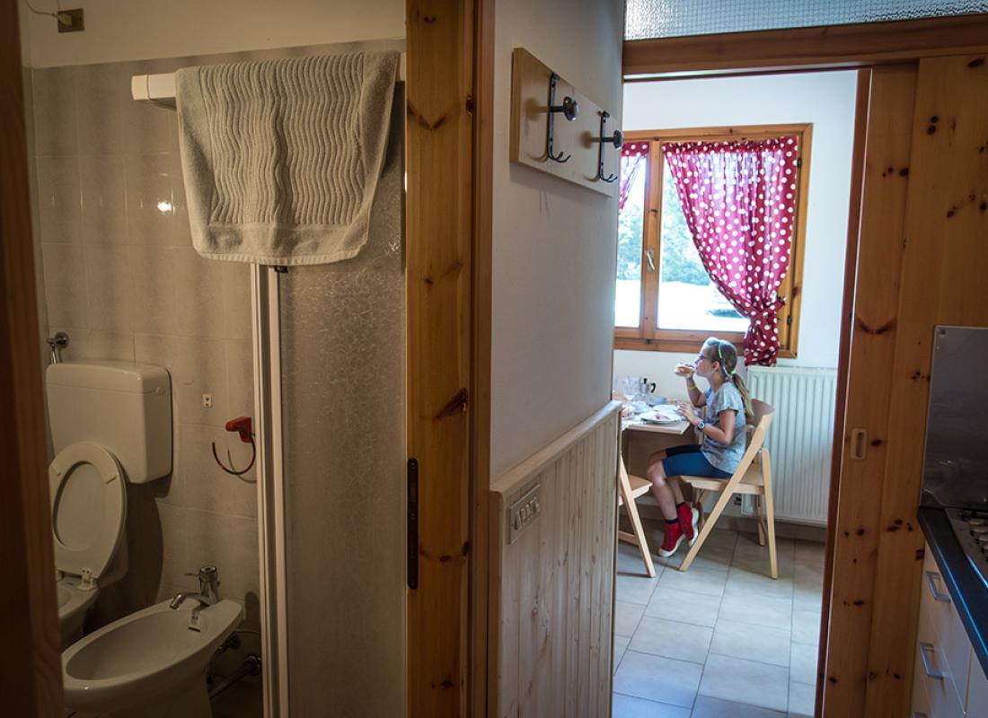 Interno con bagno e cucina, bambina seduta a tavola vicino alla finestra.