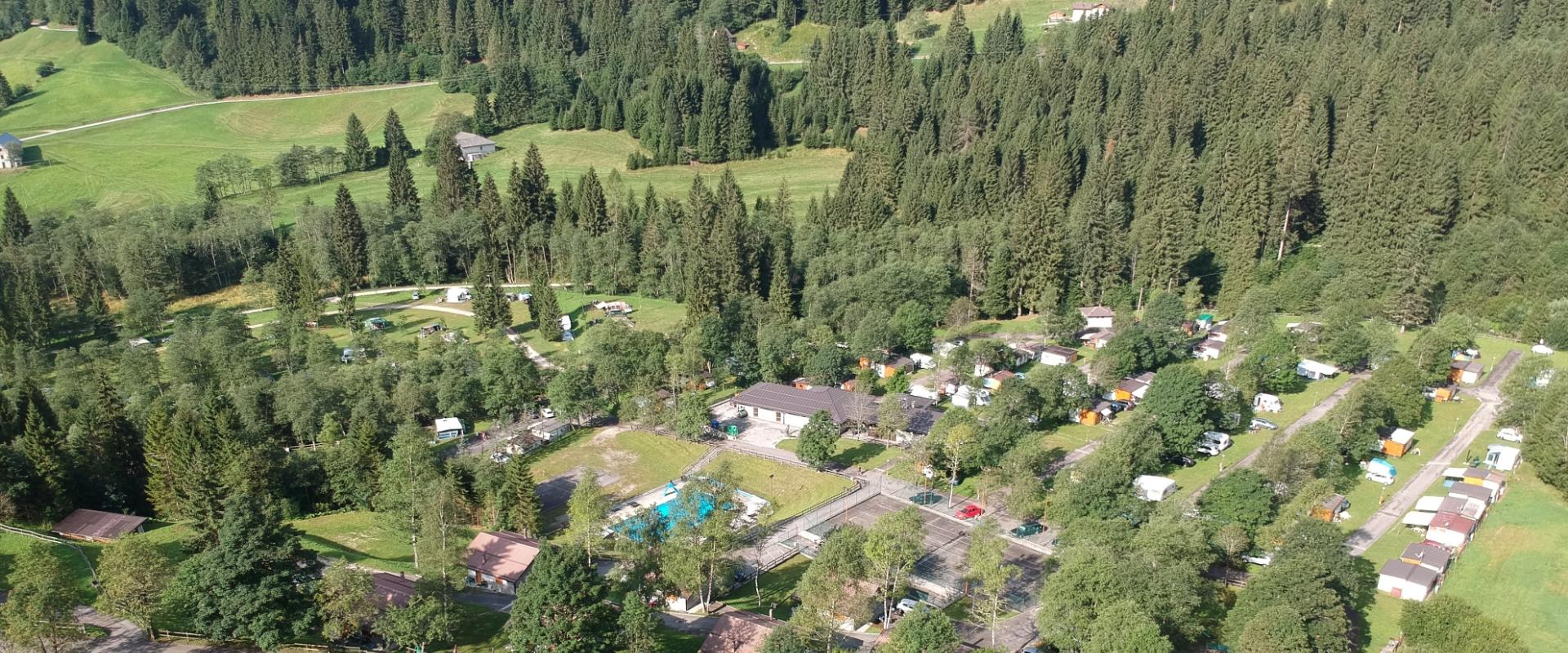 Vista aerea di un campeggio immerso nel verde con piscina e roulotte.