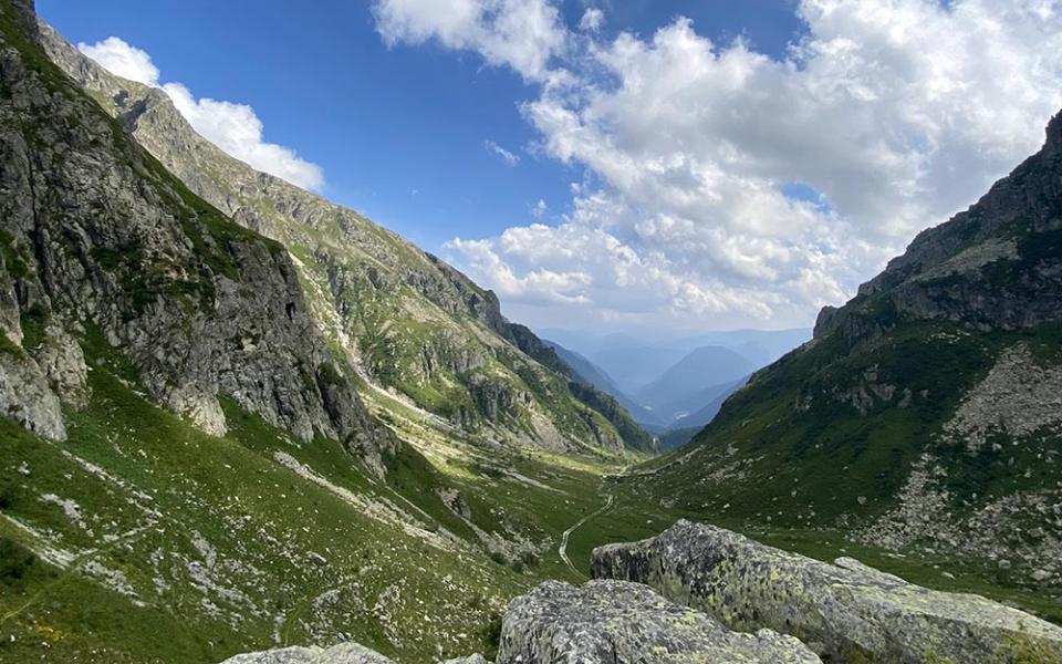 Panorama montano con cielo azzurro e nuvole, valli e rocce verdi.