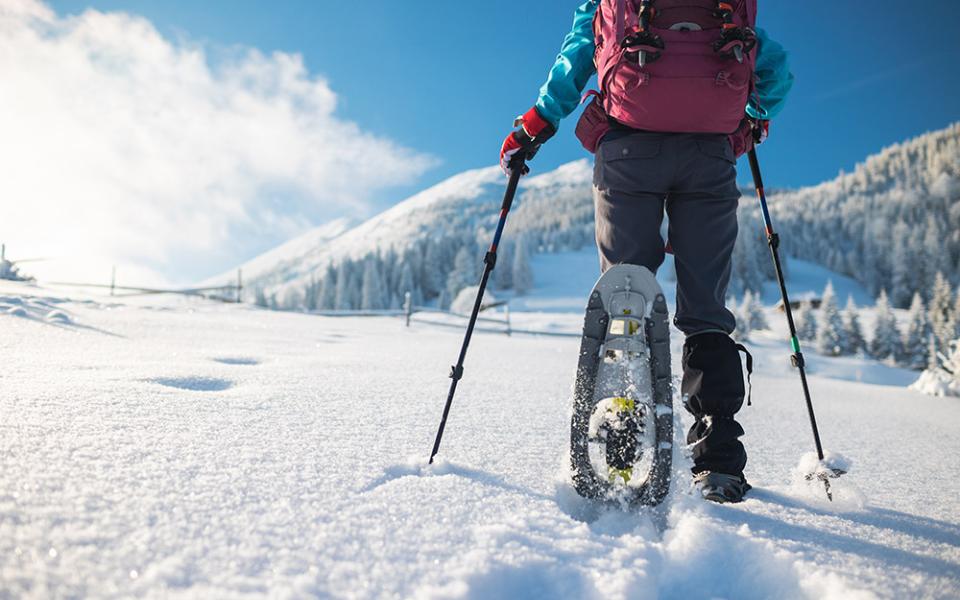 Persona con racchette da neve cammina su un paesaggio innevato e soleggiato.