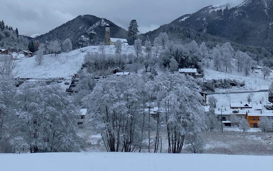Paesino montano innevato con case colorate e chiesa, circondato da montagne.