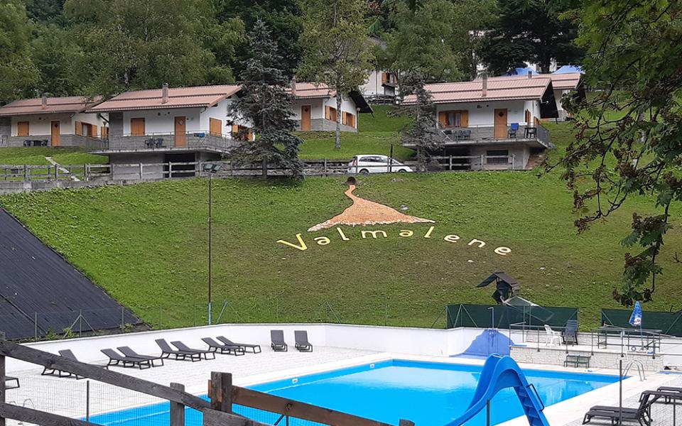 Piscina all'aperto a Valmalene con scivolo e lettini, circondata da chalet.
