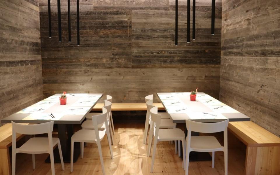Sala da pranzo moderna con tavoli bianchi, sedie e pareti in legno.