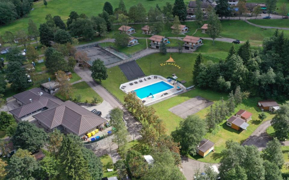 Vista aerea di un campeggio con piscina e bungalow immersi nel verde.
