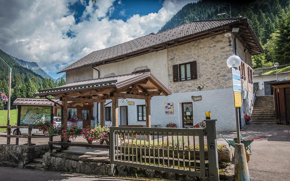 Edificio di montagna con giardino fiorito, cielo nuvoloso e sfondo alpino.
