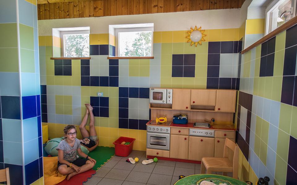 Stanza giochi per bambini con cucina giocattolo e pareti colorate, due bambini presenti.