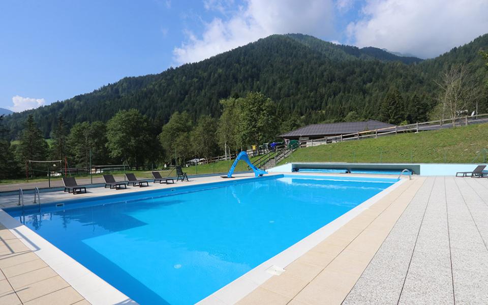 Piscina all'aperto con scivolo, circondata da montagne e lettini prendisole.
