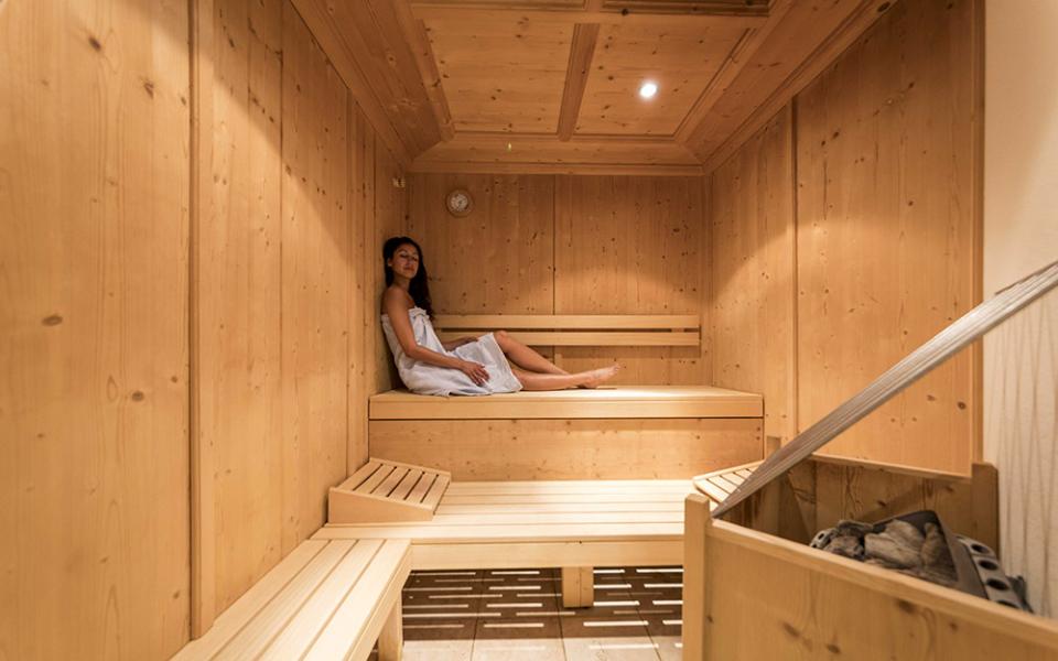 Donna rilassata in sauna di legno con asciugamano bianco.