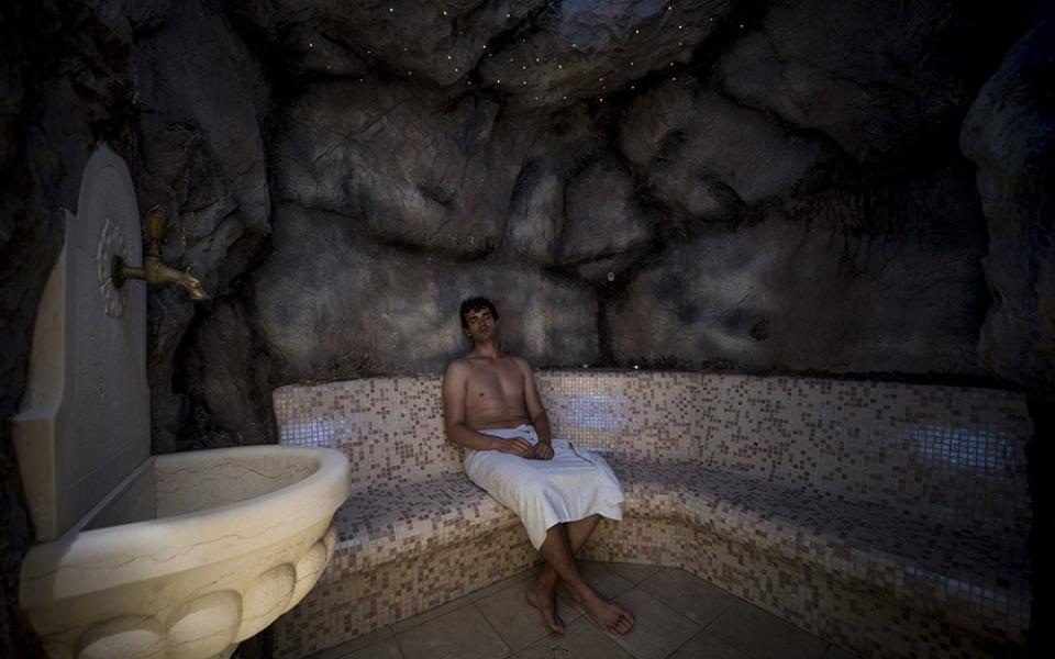 Uomo rilassato in sauna con pareti di pietra e panca a mosaico.